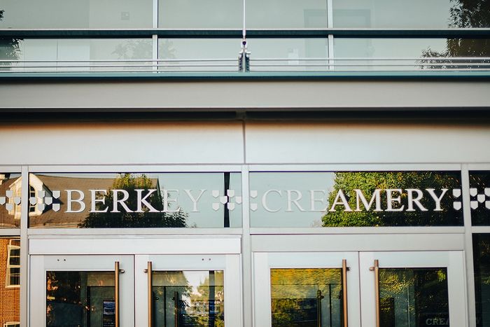 Charming storefront of Berkey Creamery with sleek glass doors and reflections of surrounding greenery.