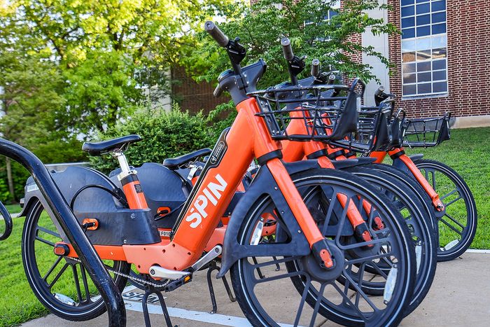 Vibrant orange rental bikes lined up in a sunny, lush green park setting, perfect for eco-friendly urban commuting.