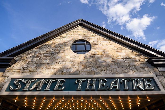Charming brick facade of State Theatre with illuminated marquee against a blue sky backdrop.