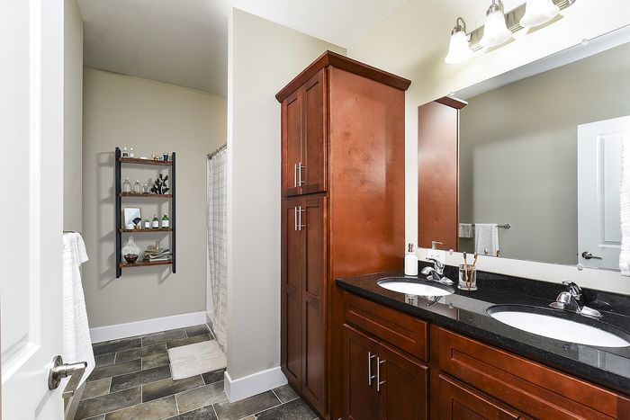 Elegant bathroom featuring dual sinks with sleek black countertop, warm cherry wood cabinets, and a stylish open shelving unit for storage.