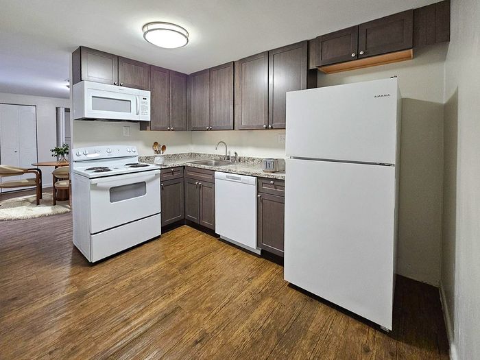 Inviting kitchen with sleek dark cabinetry, modern appliances, and warm wood flooring, leading to a cozy dining area.