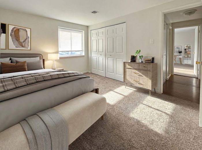 Sunlit bedroom with elegant decor, plush carpeting, modern dresser, and cozy bedding leading to an adjoining bright hallway.