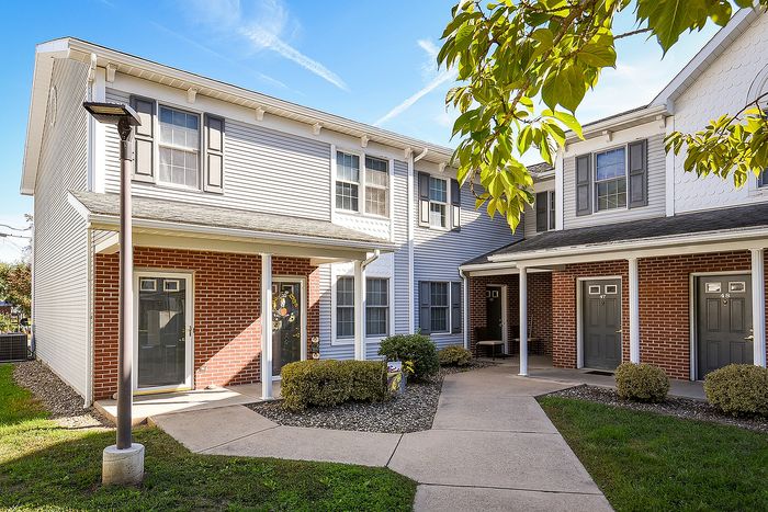 Charming townhouse exterior with classic brick and neutral siding, featuring a welcoming porch and lush greenery.