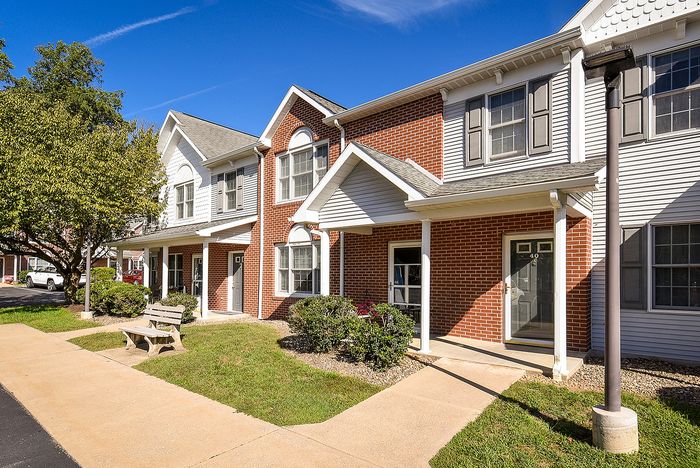 Inviting townhouse exterior with classic brick facade, charming porch, and lush landscaping under a clear blue sky.