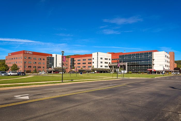 Modern medical facility with red brick facade, large windows, and expansive green lawn under a clear blue sky.