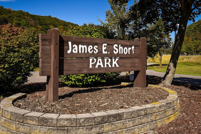 Charming wooden sign for James E. Short Park surrounded by lush greenery and a bright blue sky.