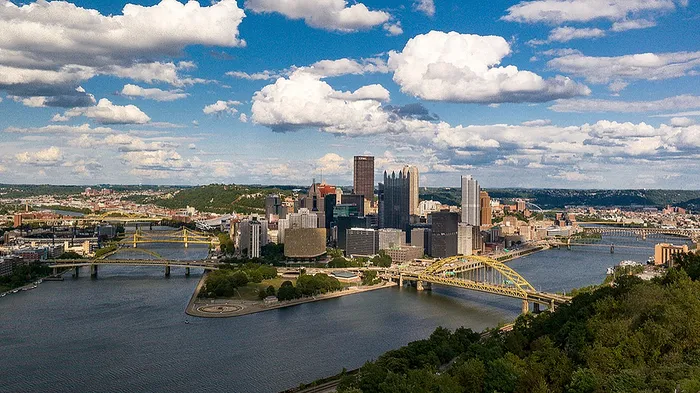 Stunning aerial view of a vibrant city skyline featuring iconic yellow bridges, surrounded by serene rivers and lush greenery under a picturesque sky.