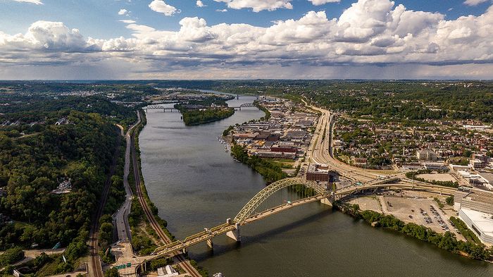 Breathtaking aerial view of a vibrant cityscape with lush greenery, winding rivers, and stunning bridges under a dramatic sky.