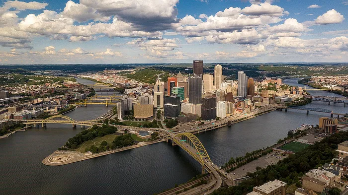 Breathtaking aerial view of a vibrant city skyline with iconic bridges crossing three winding rivers under a clear, blue sky.
