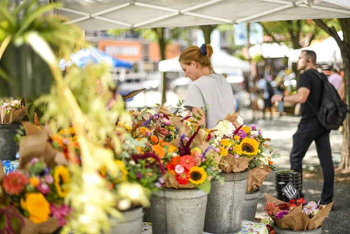Vibrant outdoor market scene with colorful flower bouquets in rustic metal buckets under a canopy, capturing the essence of a lively community space.
