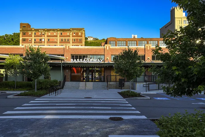 Charming brick-faced building with lush greenery and spacious walkway leading to elegant entrance under a clear blue sky.