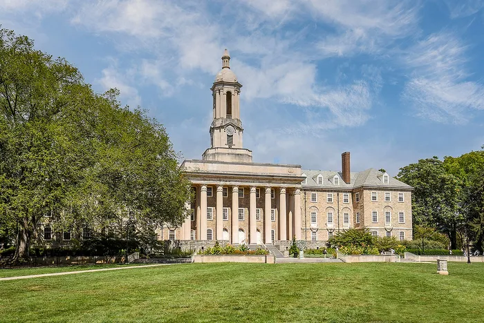 Majestic neoclassical building surrounded by lush greenery and a vibrant lawn under a bright blue sky.