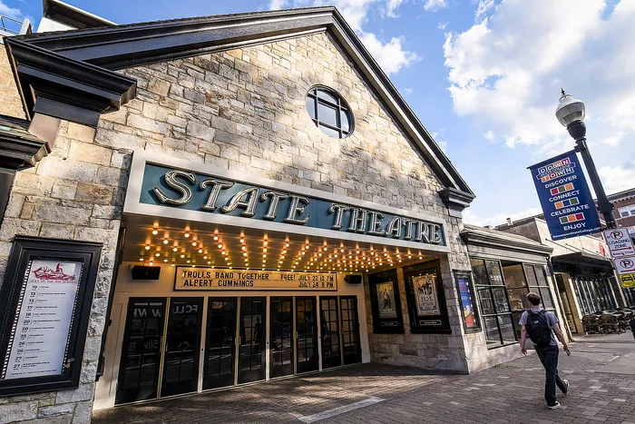 Charming stone facade of State Theatre with bright marquee lights and a welcoming entrance, set against a vibrant blue sky.