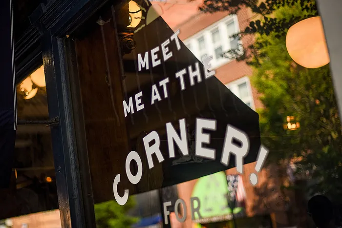 Inviting café sign reading 'Meet Me at the Corner' with warm interior lighting and urban reflections.