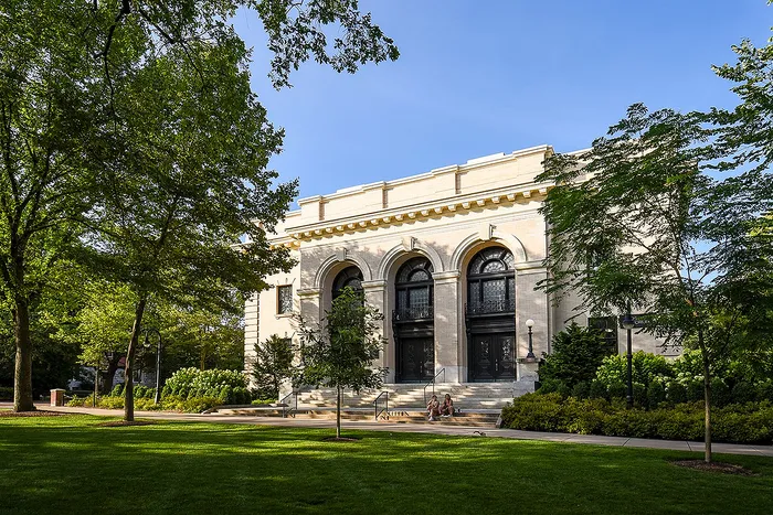 Elegant historic building with grand arches surrounded by lush greenery on a sunny day, perfect for a serene and picturesque setting.