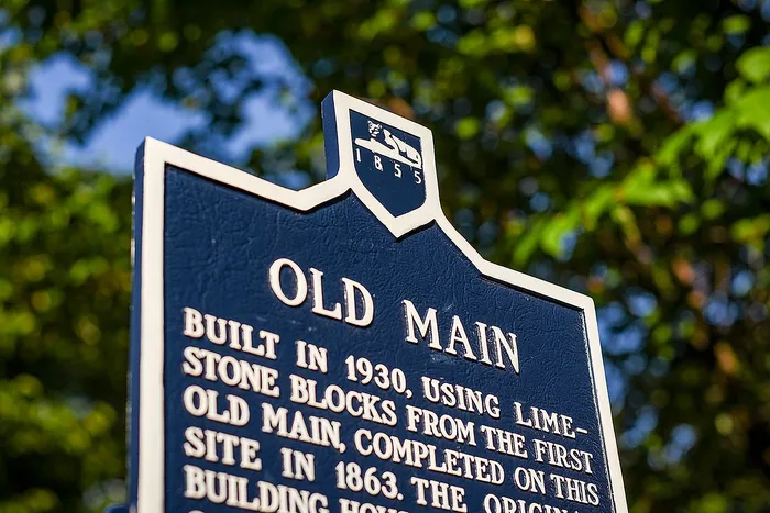 Elegant historical marker for 'Old Main' framed by lush green foliage, highlighting its 1930 limestone block construction.