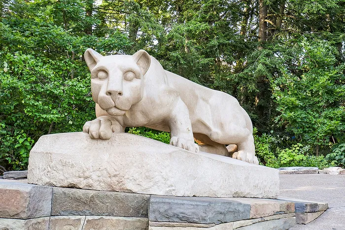 Elegant stone sculpture of a lioness gracefully poised on a pedestal surrounded by lush greenery.