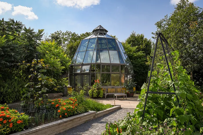 Charming glass conservatory surrounded by lush green foliage and vibrant flower gardens, creating a serene outdoor escape.
