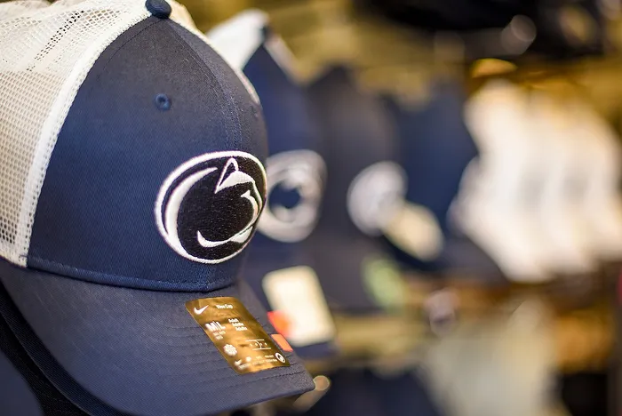 Close-up of a stylish blue and white baseball cap with a distinct embroidered logo, set against a blurred display of similar caps, showcasing sporty elegance and premium design.
