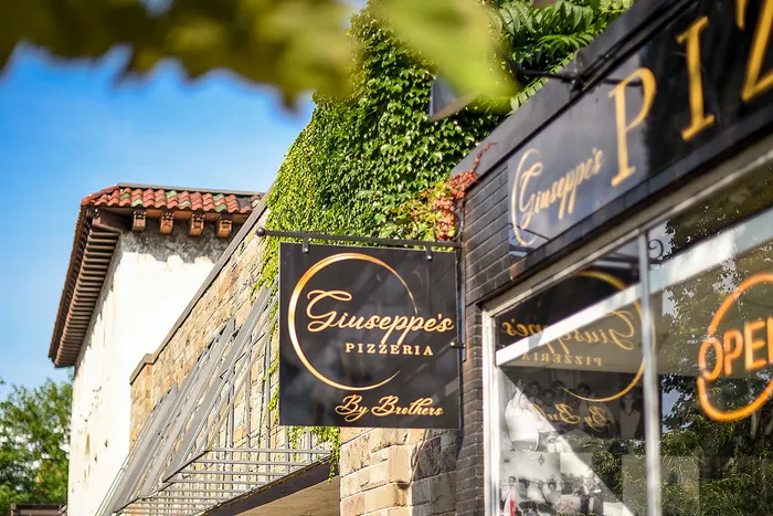 Charming pizzeria storefront with elegant signage and lush green ivy, hinting at a welcoming dining experience.