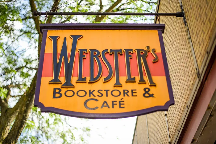 Inviting bookstore and café sign with vibrant colors, nestled under lush tree canopy.