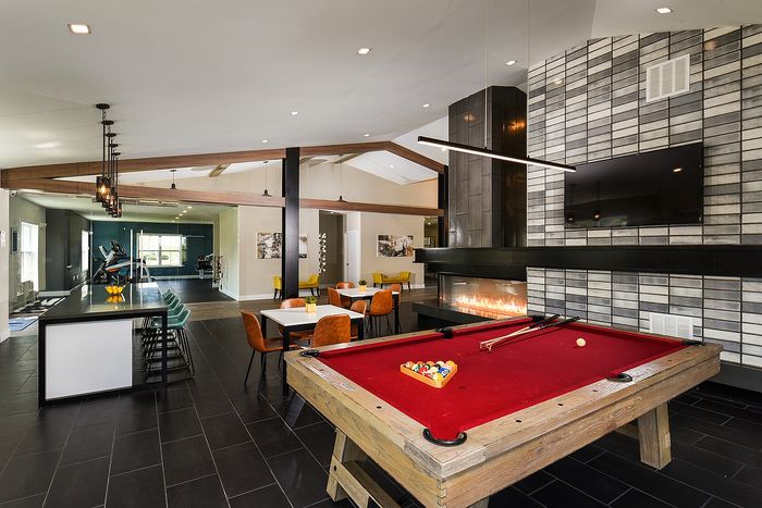 Modern open living area with a red pool table, cozy fireplace, stylish seating, and a sleek workout space.