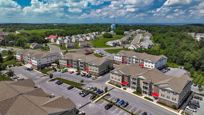 Scenic aerial view of modern apartment complex with well-maintained buildings, ample parking, and lush green surroundings.