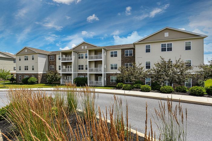 Charming apartment complex with balconies, lush greenery, and a sunny courtyard set against a bright blue sky.