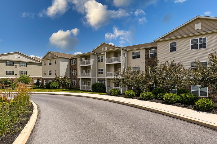 Charming apartment complex with a stunning facade, surrounded by lush greenery and a welcoming pathway under a bright blue sky.
