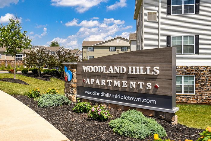 Inviting Woodland Hills Apartments sign with charming landscaping and modern architecture under a sunny blue sky.