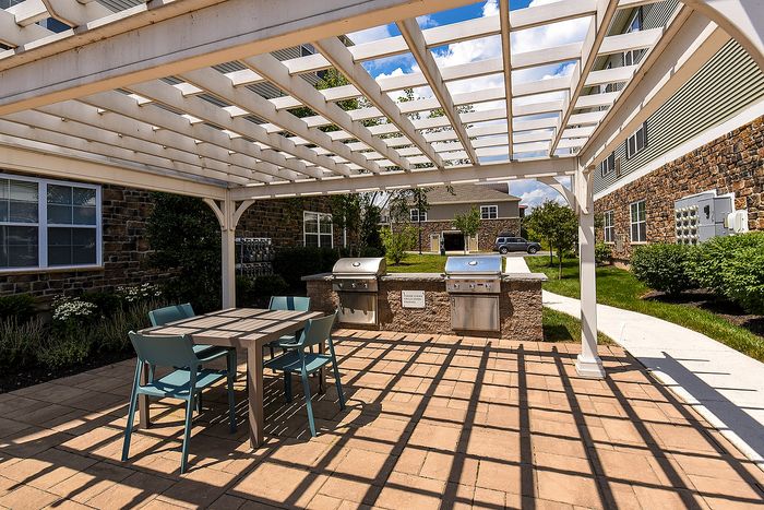 Charming outdoor patio with stylish pergola, seating area, and modern grilling stations in a landscaped apartment community.
