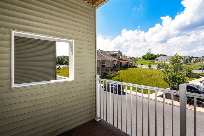 Charming balcony view of a peaceful suburban street with lush greenery and cozy homes under a bright blue sky.