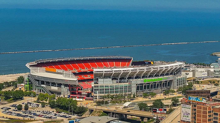 Breathtaking aerial view of a large waterfront stadium, highlighting its vibrant red seating and modern architecture with an expansive view of the shimmering blue lake in the background.
