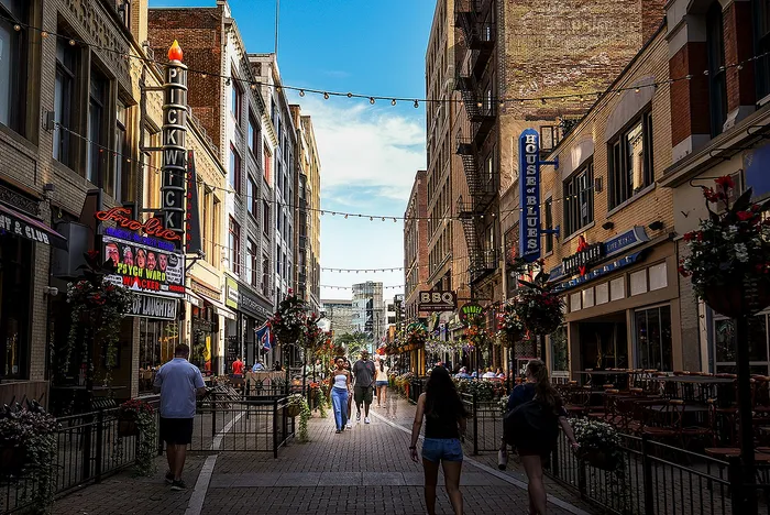 Vibrant urban street filled with lively restaurants, colorful signs, and people enjoying a sunny day.