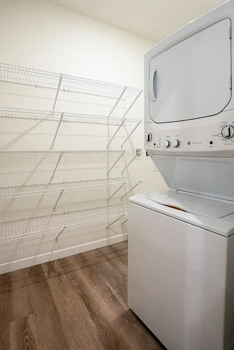 Efficient laundry area with a modern stacked washer and dryer, featuring sleek wire shelving and elegant wooden flooring, optimizing space and functionality.