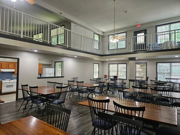 Inviting apartment community space featuring elegant wooden tables, chic black chairs, and a stylish loft area with abundant natural light.