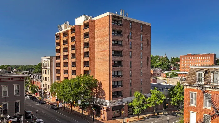Charming urban apartment building with brick facade surrounded by lush greenery and a vibrant neighborhood view under a clear blue sky.