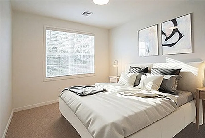Bright and inviting bedroom with a large window, elegant artwork, and cozy bedding in a modern apartment.