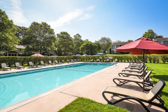 Inviting outdoor pool with surrounding lounge chairs and vibrant red umbrellas, perfect for relaxation and enjoyment.