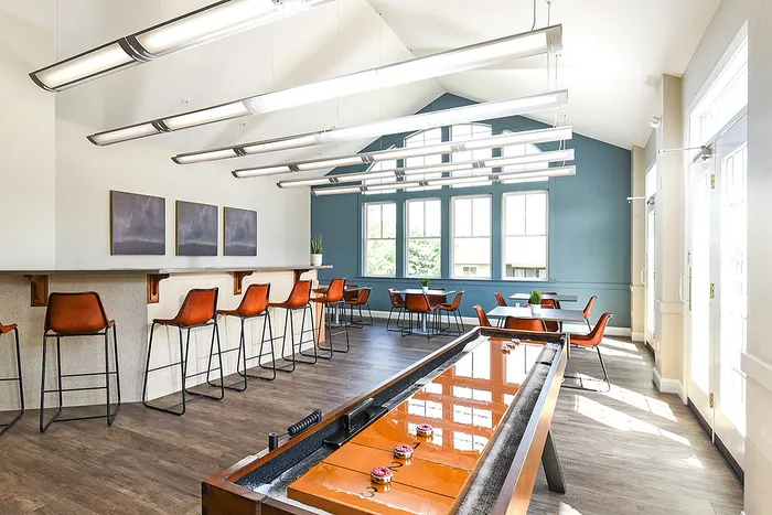 Bright and modern communal area with stylish bar seating, gaming table, and elegant windows providing ample natural light.