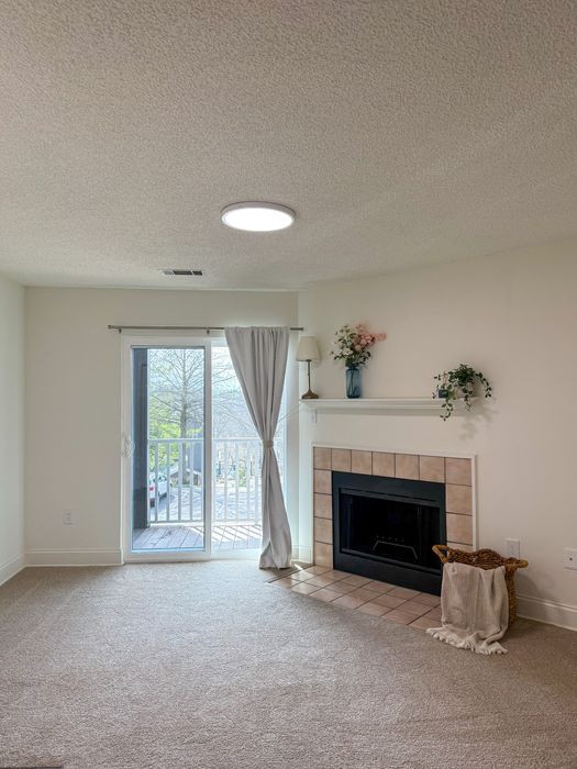 Inviting living room with plush carpet, elegant fireplace, and natural light streaming through glass doors leading to a charming balcony.