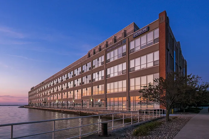 Stunning waterfront building at sunset with large windows reflecting the vibrant sky; ideal location for modern apartments.