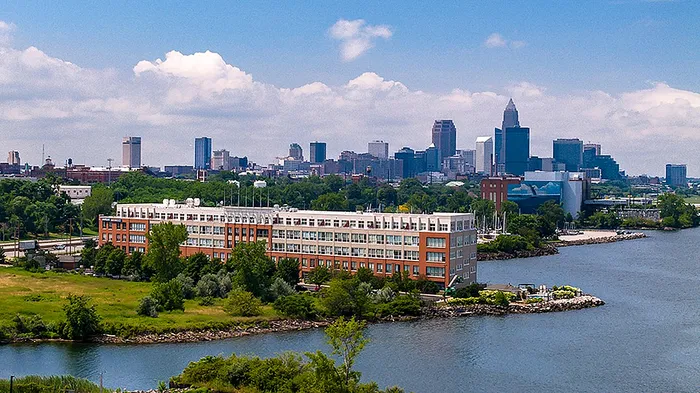 Panoramic aerial view of a modern waterside apartment complex with lush greenery and a striking city skyline backdrop.