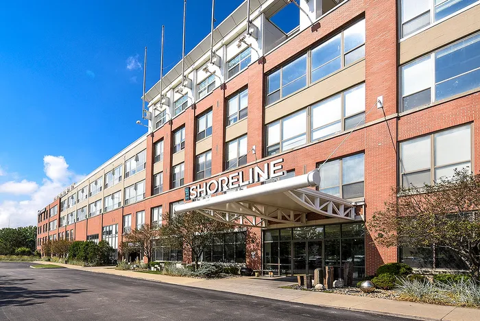 Impressive facade of The Shoreline apartment building, showcasing modern architecture with large windows and a welcoming entrance, bathed in bright sunlight.