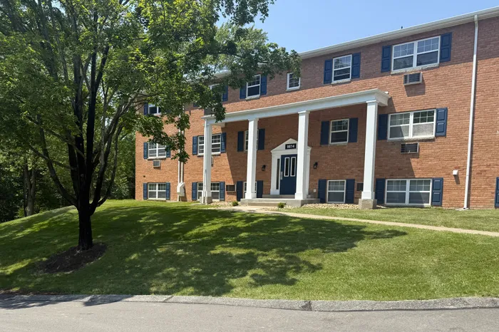 Charming brick apartment building with elegant columns and lush green surroundings, ideal for serene living.