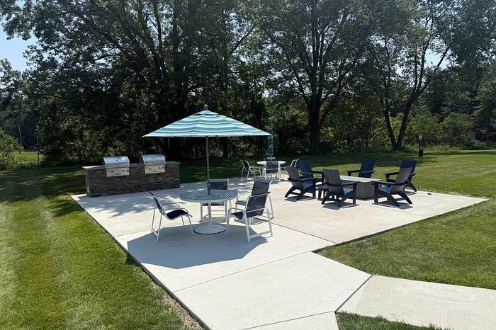 Charming outdoor patio with stylish seating, barbecue grills, and a colorful umbrella, surrounded by lush greenery.