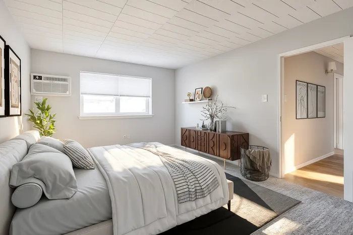 Bright and airy bedroom featuring sleek furniture and a modern aesthetic, enhanced by natural light streaming through a large window.