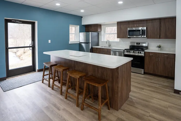 Modern kitchen with sleek wooden cabinetry, stainless steel appliances, and a spacious island with bar seating, accented by a stylish blue wall and natural light.