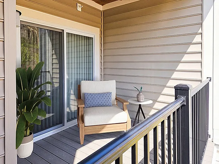 Charming apartment balcony featuring cozy seating, lush potted plant, and serene outdoor views, perfect for relaxation.