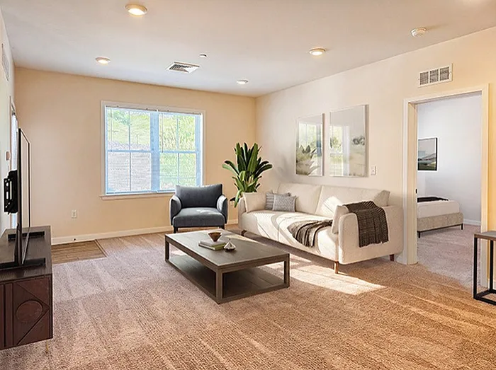 Inviting living room with plush carpeting, elegant decor, and abundant natural light from a large window, leading into a cozy bedroom.